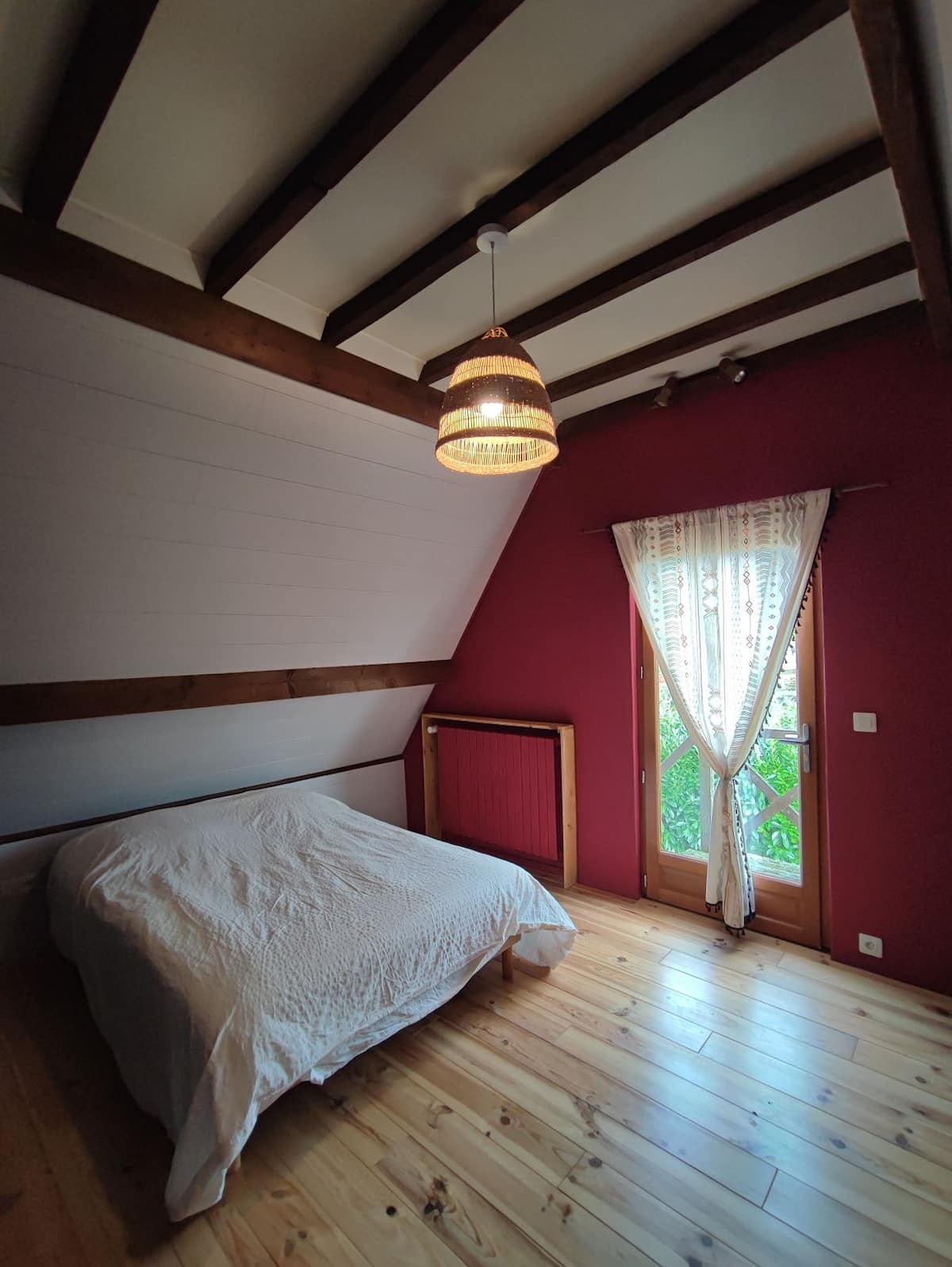 Chambre mansardée avec mur rouge, poutres apparentes et grand lit
