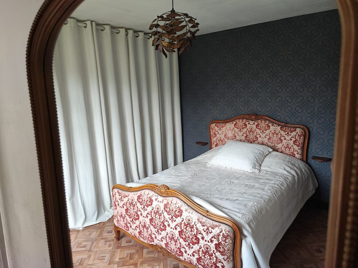 Chambre tapissée de bleu avec lit ancien et tête de lit damassée
